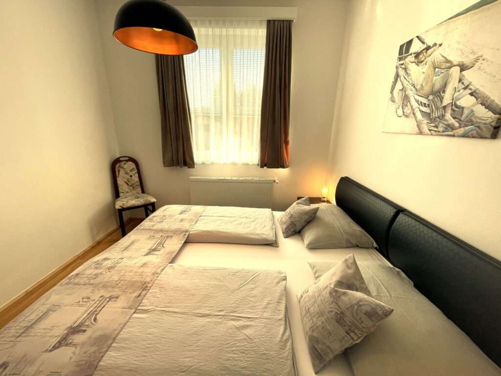 Schlafzimmer mit schwarzem Lederbett, Sessel in der Ecke und Terrence Hill Bild an der Wand